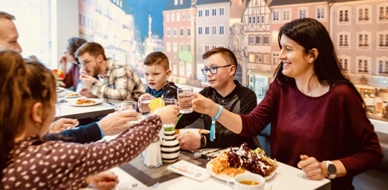 Beste Verpflegung beim Familienurlaub in der Jugendherberge Eine Familie im Restaurant der Jugendherberge Trier. Die Eltern sitzen mit den Kindern an Tisch und stoßen mit gefüllten Glasen an.