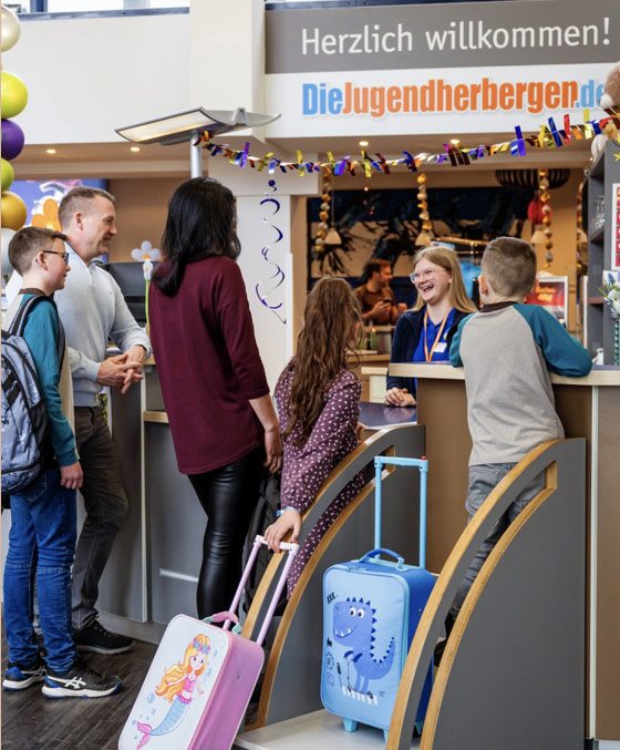 Beste Verpflegung beim Familienurlaub in der Jugendherberge Eine Familie im Restaurant der Jugendherberge Trier. Die Eltern sitzen mit den Kindern an Tisch und stoßen mit gefüllten Glasen an.